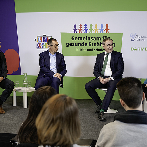 Foto von vier Erwachsenen, die auf der Bühne der Pressekonferenz sitzen und miteinander sprechen